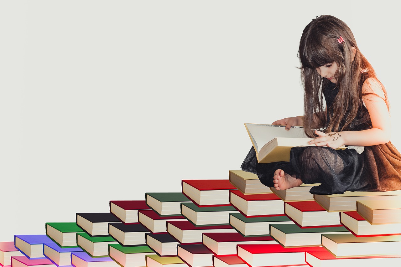 山積みの本の上で読書する少女